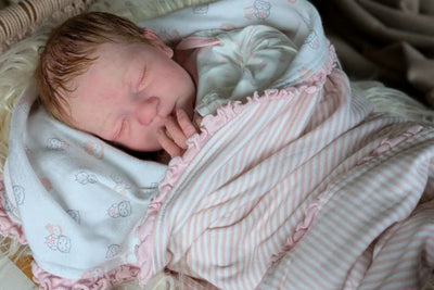 Reborn baby doll peacefully resting while wrapped in a soft blanket, lying down with a calm expression