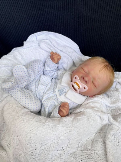 Reborn Doll Milan with ultra-realistic details, Genesis paint, and premium hand-rooted hair, lying down with a magnetic pacifier.